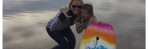 Bailey and Ellie holding a skating board at the beach