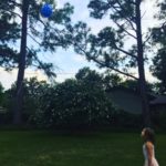 Ellie is playing with the blue color balloon in the backyard